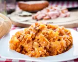 Pyszny bigos Ani, gotowany z pasją, na talerzu. Obok bułka i kawałki kiełbasy.