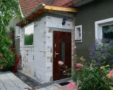 Budowa nowego przedsionka do domu bez pozwolenia. Białe pustaki, brązowe drzwi i okno czekają na wykończenie.