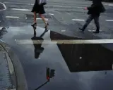 Jay Maisel photography captures a rainy street scene with blurred figures crossing, their reflections distorted in puddles, mirroring the city's mood.