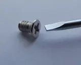 Tornillo metálico con cabeza de estrella y destornillador plano listo para ayudar a como quitar un tornillo pasado.