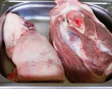 Deux morceaux de viande crue, dont une belle rouelle de porc, reposent dans un bac en métal.