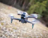 Eine FPV Drohne fliegt über steinigen Boden. Sie hat eine Kamera vorne und leuchtende blaue Lichter an den Armen.