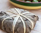 Un mets emballé dans des feuilles séchées, lié par des brins, évoquant les spécialités des Hautes-Alpes.