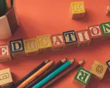 Klocki z literami tworzą napis EDUCATION. Obok leżą kredki i inne klocki, idealne do nauki tekstów po angielsku B2.