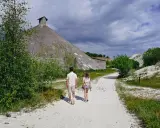 Två personer går på en grusväg mot en stor, konformad byggnad. Omgivningen påminner om vita klippor i Danmark, med grönska och en dramatisk himmel.