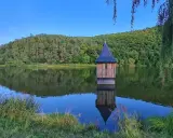 Holzhaus mit spitzem Dach, wie eine kleine Kirche im See, spiegelt sich im ruhigen Wasser.
