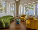 Salotto con divano verde curvo e poltrone gialle, tavolini di design e vista lago. Un'elegante casa Art Déco.
