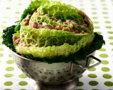 Un chou farci, recette traditionnelle, présenté dans une passoire en métal. Les feuilles de chou vert vif enrobent une garniture de viande hachée.