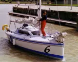 Un homme en salopette rouge prépare un voilier coco, le numéro 6 bien visible sur la proue, prêt à naviguer sur un canal.