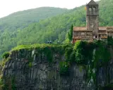 Castillo medieval en un acantilado, uno de los pueblos de Girona, rodeado de vegetación exuberante.