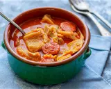 Un cuenco verde con callos a la madrileña, trozos de chorizo y un tenedor.