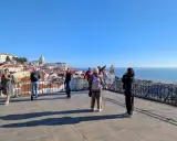 Blick vom Miradouro Portas do Sol auf Lissabons Dächer und das Meer. Touristen genießen die Aussicht.