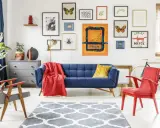 Salon w stylu eklektycznym: granatowa kanapa, czerwony fotel, dywan z geometrycznym wzorem i galeria obrazów na ścianie.