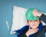 Chory chłopiec z okładem na głowie i termometrem obok. Podpowiadamy, jak zbić gorączkę u dziecka domowym sposobem.