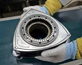 Rotor silnika Wankla, kluczowy element innowacyjnych samochodów z silnikiem Wankla, trzymany w rękawiczkach.
