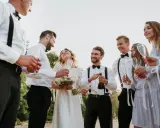 Pan młody i świadek świętują z panną młodą i druhnami. Wszyscy uśmiechnięci, w rękach kieliszki i butelka szampana.