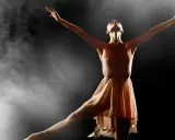 En ballerina i en ljusrosa klänning utför en graciös rörelse i klassisk balett, omgiven av dramatisk rök och ljus.