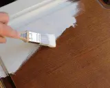 Mano pintando una puerta de madera con brocha blanca. Guía para como pintar puertas de madera.