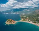Malownicza wyspa Sveti Stefan, połączona z lądem piaszczystą mierzeją, otoczona turkusowym morzem i górami.