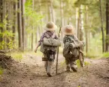 Dwoje dzieci w kapeluszach i z plecakami wyrusza na leśną ścieżkę. To przygoda i nauka survivalu dla dzieci.