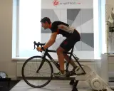 Mann auf einem Rennrad-Trainer, der sein Lungenvolumen trainiert. Hinter ihm eine Wand mit Triathlon-Logo und Messmarkierungen.