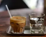Kawa z lodem i słomką obok szklanki wody. Czy kawa jest moczopędna? Z's Cafe.