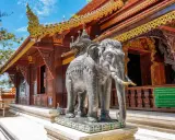 Chiang Mai atrakcje: kamienny słoń przed ozdobną świątynią z bogato zdobionym dachem.