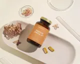 Butelka z suplementem omega 3 dla niemowląt, dwie kapsułki i suszone kwiaty na ceramicznej tacce.