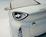 Dettaglio di un'auto elettrica Smart, con un faro futuristico e il logo dorato. Nuovi modelli in arrivo.