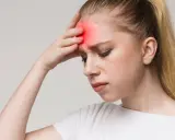 Junge Frau mit Stirnband, das starke Kopfschmerzen nach dem Aufwachen zeigt.