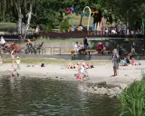 Rodzina odpoczywa nad wodą na piaszczystej plaży Jeziora Paprocany. Dzieci bawią się w piasku i przy brzegu, dorośli relaksują się na kocach i ławkach.
