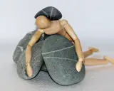 Drewniany ludzik przygnieciony kamieniami, symbolizujący abulię – brak woli i motywacji do działania.