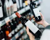 Manos sostienen botellas de vino tinto, eligiendo entre los vinos más vendidos en España.