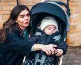 Mama pokazuje coś dziecku w najmniejszej spacerówce. Maluch w czapce i kurtce wygląda ciekawie.