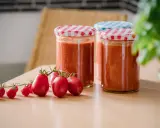 Frische Tomaten und eingekochte Tomatensauce in Gläsern. Die Frage "Tomatensauce einkochen wie lange?" beschäftigt viele Hobbyköche.