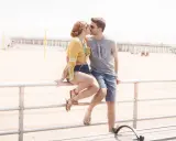 Para całuje się na plaży, siedząc na barierce. Ich bliskość pokazuje zdrowe granice w związku, pełne zaufania i czułości.