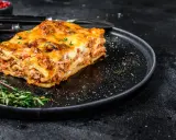 En bit gyllene lasagne på en svart tallrik, perfekt comfort food med köttfärs och ost.