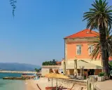 Słoneczny dzień na plaży na półwyspie Pelješac. Palmy, kamienny murek, tawerna i turkusowe morze.
