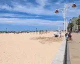 Sonniger Tag am Playa Victoria in Cádiz. Menschen entspannen sich unter bunten Sonnenschirmen, während Kinder am Strand spielen.