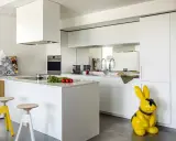 Cucina moderna con isola centrale e sgabelli. La differenza tra RAL 9003 e 9010 è sottile, ma qui il bianco puro domina, con un tocco di giallo dato da un coniglio decorativo.