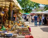 Bunte Lampen, Keramik und Textilien auf einem orientalischen Warenmarkt. Menschen schlendern zwischen den Ständen hindurch.