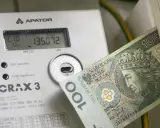 Licznik energii elektrycznej z banknotem 100 zł. Wysokie rachunki za prąd to problem, ale dodatek energetyczny może pomóc.
