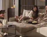 Två vänner myser i en stor sov fåtölj med popcorn och filtar.