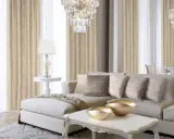 Elegancki salon w stylu nowojorskim wnętrza: beżowa kanapa, kryształowy żyrandol, złote misy i wzorzyste zasłony tworzą luksusową atmosferę.