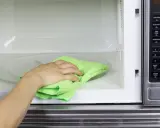 Mano con paño verde limpiando el interior de un microondas.