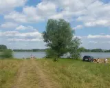 Słoneczny dzień nad jeziorem przeczyckim. Ludzie odpoczywają na trawie, w tle widać wodę i drzewa.