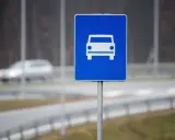 Znak drogowy szybkiego ruchu z symbolem samochodu. W tle widać rozmazany pojazd na drodze.