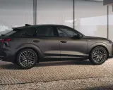 Elegancki Audi Q3 2025 w ciemnym kolorze, z dynamiczną linią nadwozia, prezentuje się na tle nowoczesnej architektury.