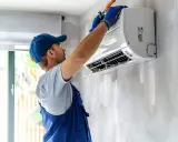 Technicien en bleu ajustant un évaporateur clim mural.