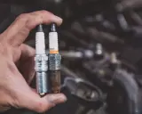 Mano sostiene bujía nueva y usada, mostrando el resultado del cambio de bujías.